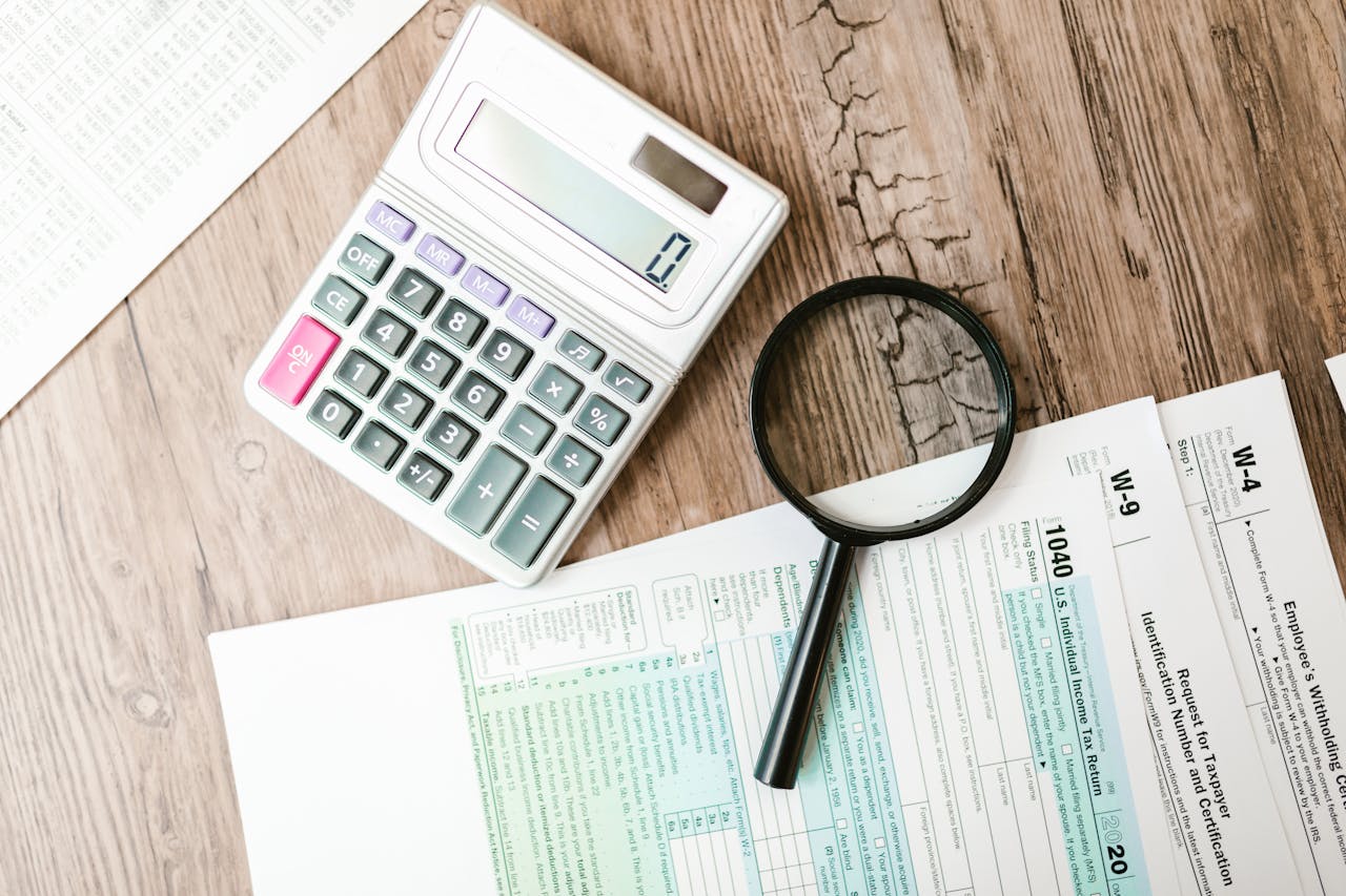 home-services-03 Tax forms laid out with a calculator and magnifying glass on a wooden surface, perfect for finance themes.